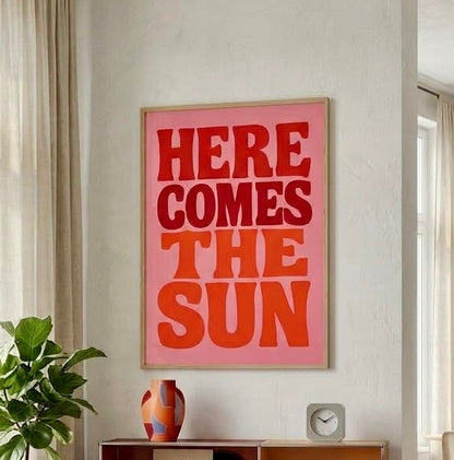 Vue rapprochée de l'affiche Here Comes The Sun au mur, cadre et lettres arrondies style années 70