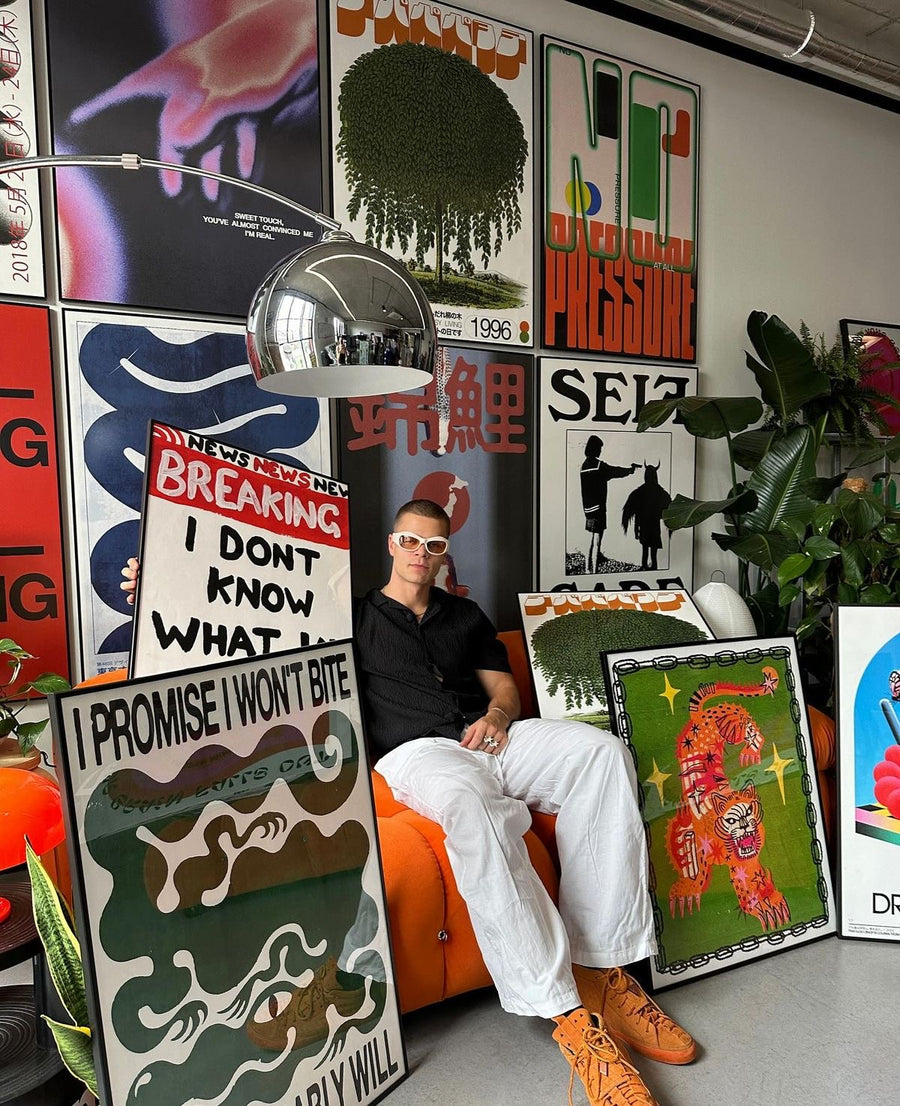 Artiste posé parmi plusieurs affiches encadrées, dont L'Œil du Tigre, dans son atelier