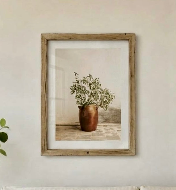 Affiche photo d'olivier encadrée sur un mur de salon, vue rapprochée de la jarre cuivrée et des branches vert argenté