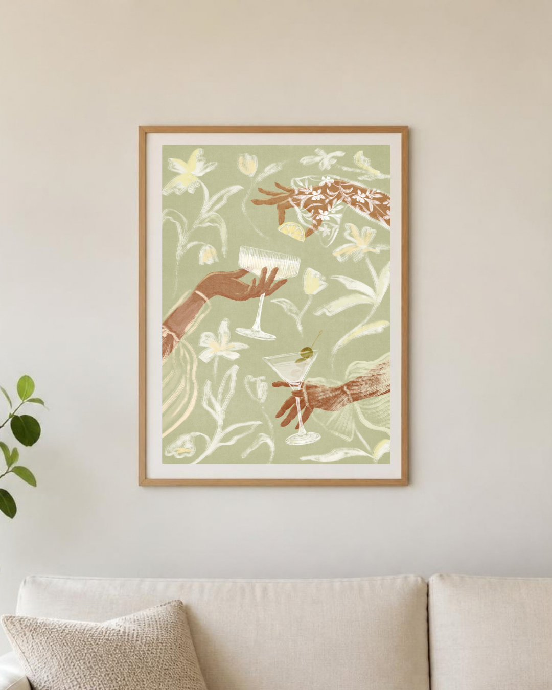 Affiche cocktails encadrée sur un mur de cuisine, vue rapprochée des mains et des verres sur fond vert sauge