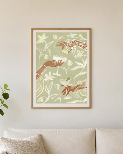 Affiche cocktails encadrée sur un mur de cuisine, vue rapprochée des mains et des verres sur fond vert sauge