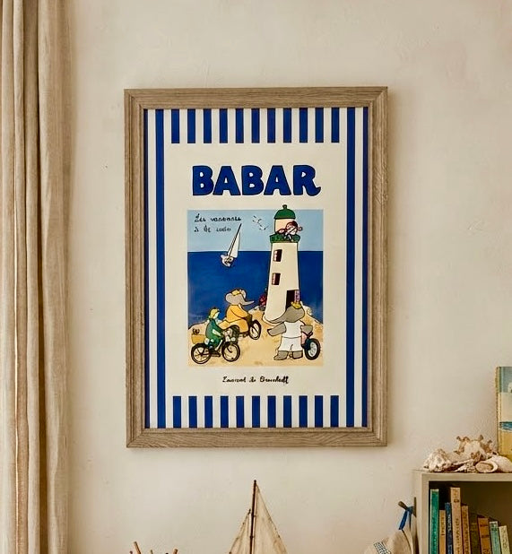 Vue rapprochée de l'affiche Babar vacances à la mer encadrée : Babar à vélo, phare blanc et mer bleue